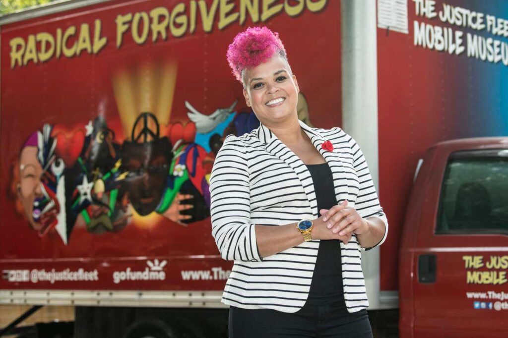 Amber Johnson, PhD, stands in front of a red box truck. "Justice Fleet Mobile Museum" and "Radical Forgiveness" are painted on the truck.