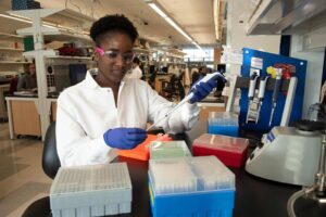 A Black woman in a basic science lab uses a pipette