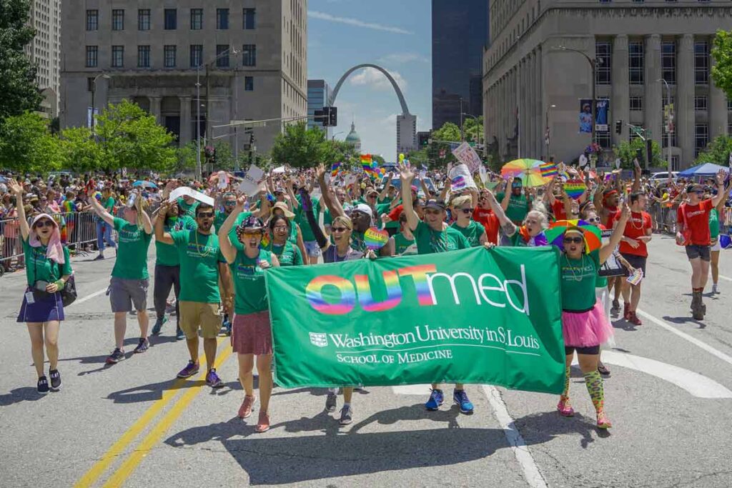 Students, faculty and staff march behind at green banner that says OUTmed at parade during Pride St. Louis